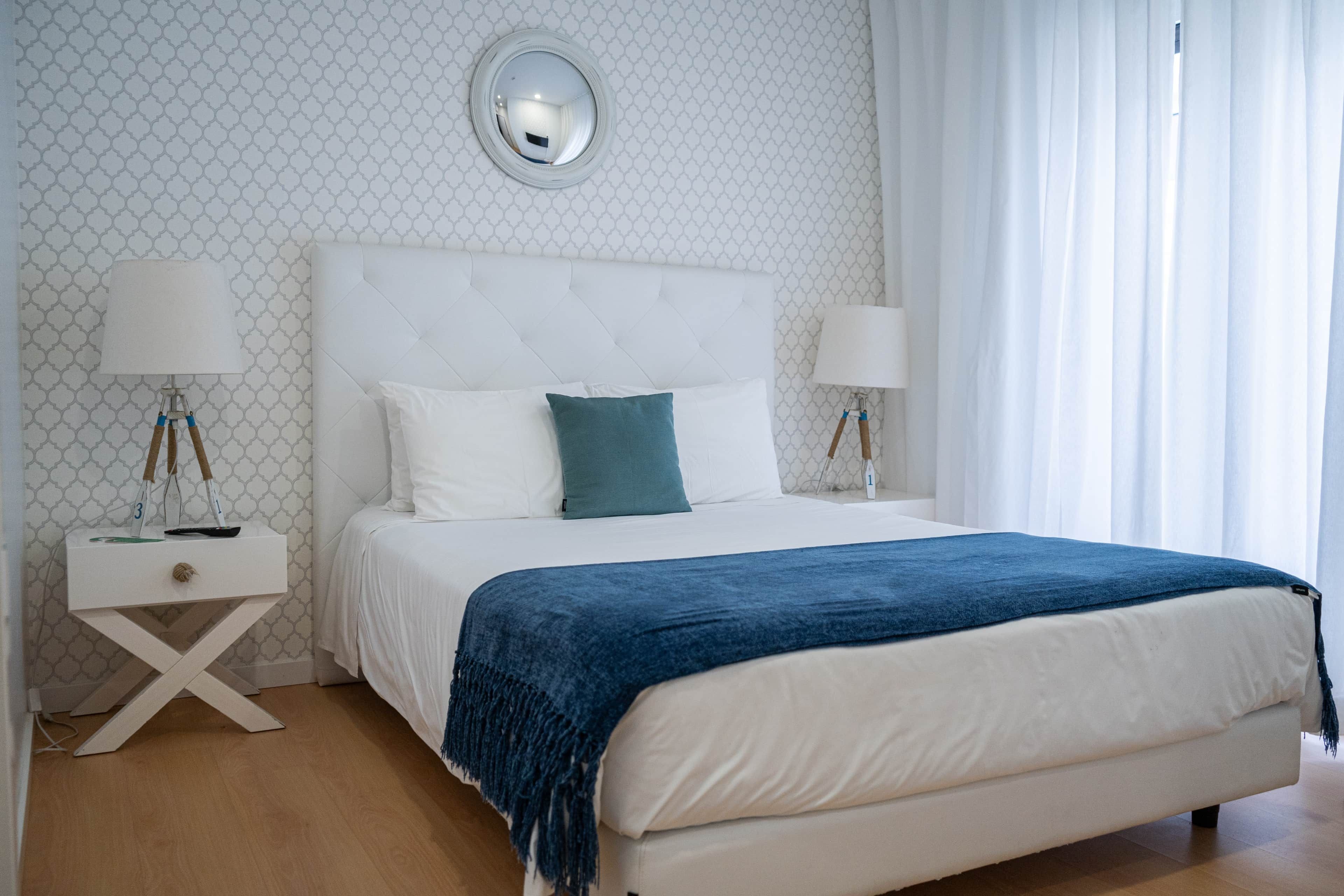 A neatly arranged bedroom with a bed, two bedside tables, and a round mirror on the wall.