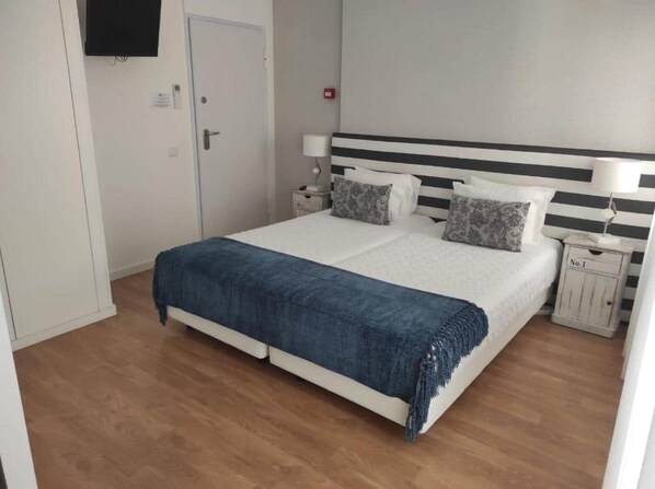 A bedroom with a bed, bedside tables, a TV, and a door. - Double Triple Suite with Balcony and Side Ocean View (Nazaré)