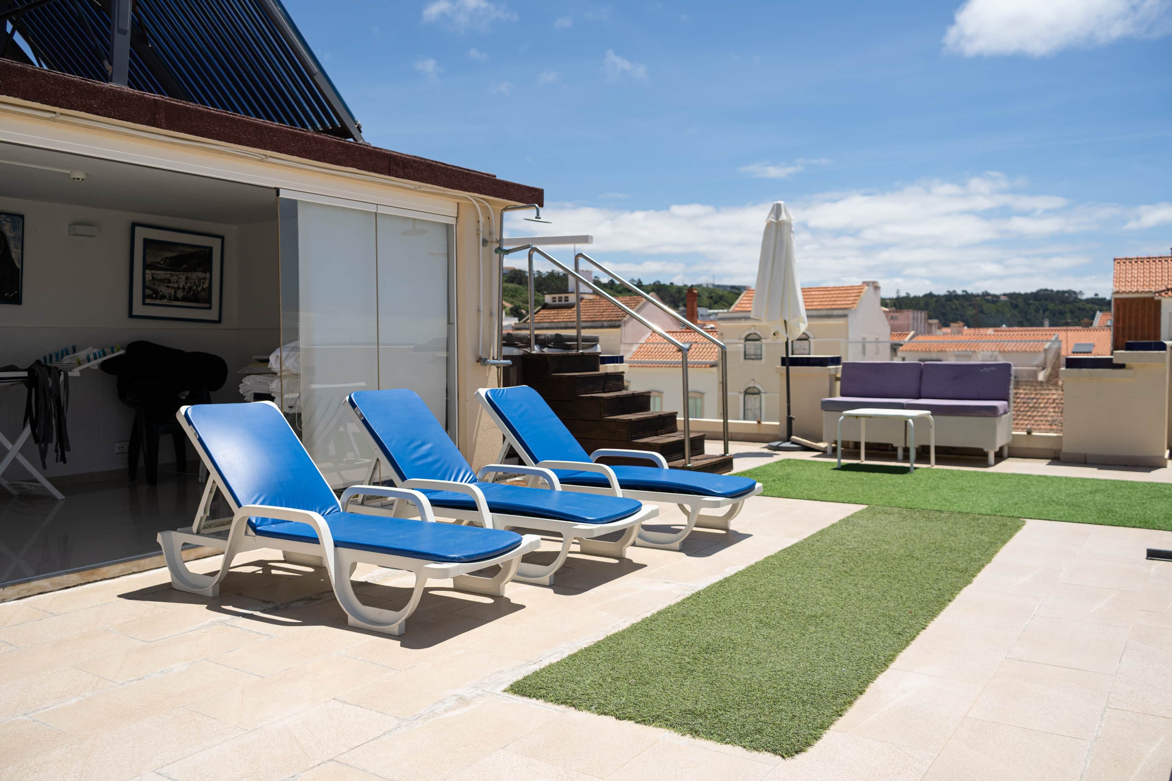 A rooftop terrace with lounge chairs, a small table, and a grassy area.