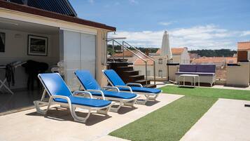 A rooftop terrace with lounge chairs, a small table, and a grassy area.