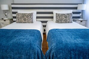 A hotel room with two beds, each with a blue bedspread and matching pillows. - Double Triple Suite with Balcony and Side Ocean View (Nazaré)