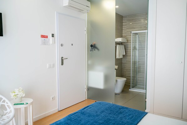 A hotel room with a bed, a small table with a plant, a shower, and a toilet.