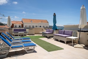 A rooftop terrace with lounge chairs, a small table, and umbrellas.
