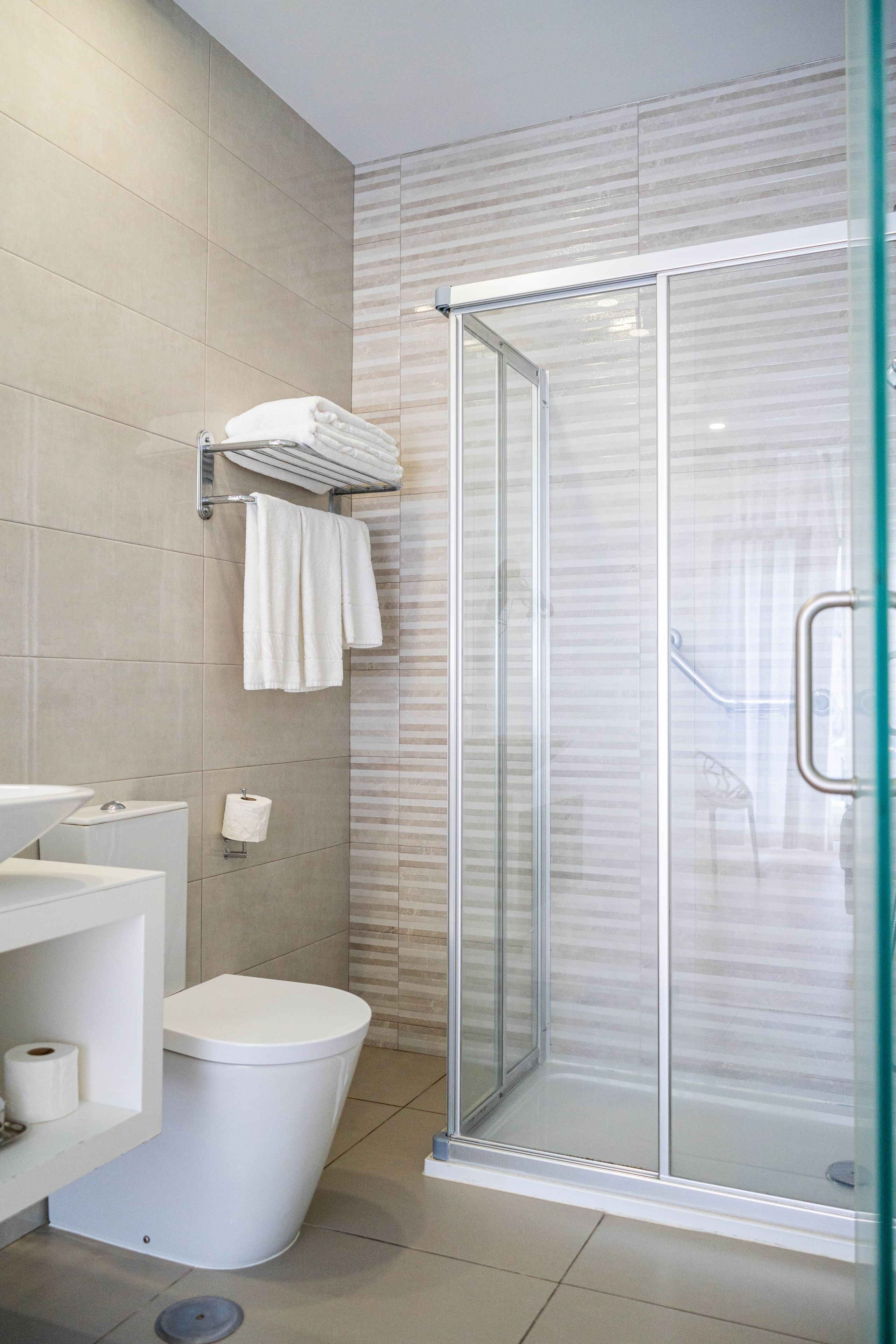 Ein modernes Badezimmer mit einer gläsernen Duschkabine, einer Toilette und einem Waschbecken mit Handtuchhalter.