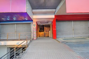 Un edificio comercial con escaparates cerrados y con persianas, una entrada central y una escalera que sube a un nivel superior.