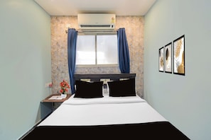 Una habitación de hotel con cama, mesita de noche, ventana con cortinas, aire acondicionado y cuadros en la pared.