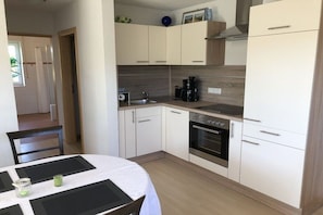 Eine kompakte Küche mit weißen Schränken, einem eingebauten Backofen und einer Kaffeemaschine.
