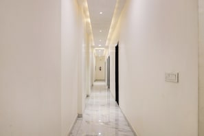 A corridor with white walls, a marble floor, and recessed lighting.