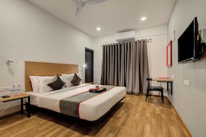A hotel room with a bed, bedside table, a desk with a chair, a flat-screen TV mounted on the wall, and a window with curtains. - Hotel O Evergreen (Faridabad)