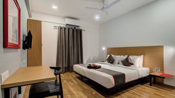 A hotel room with a bed, a desk, a chair, a ceiling fan, and a window with curtains.