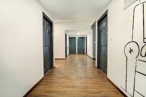 A hallway with wooden flooring, dark doors, and a wall with a simple line drawing. - Hotel O Evergreen (Faridabad)