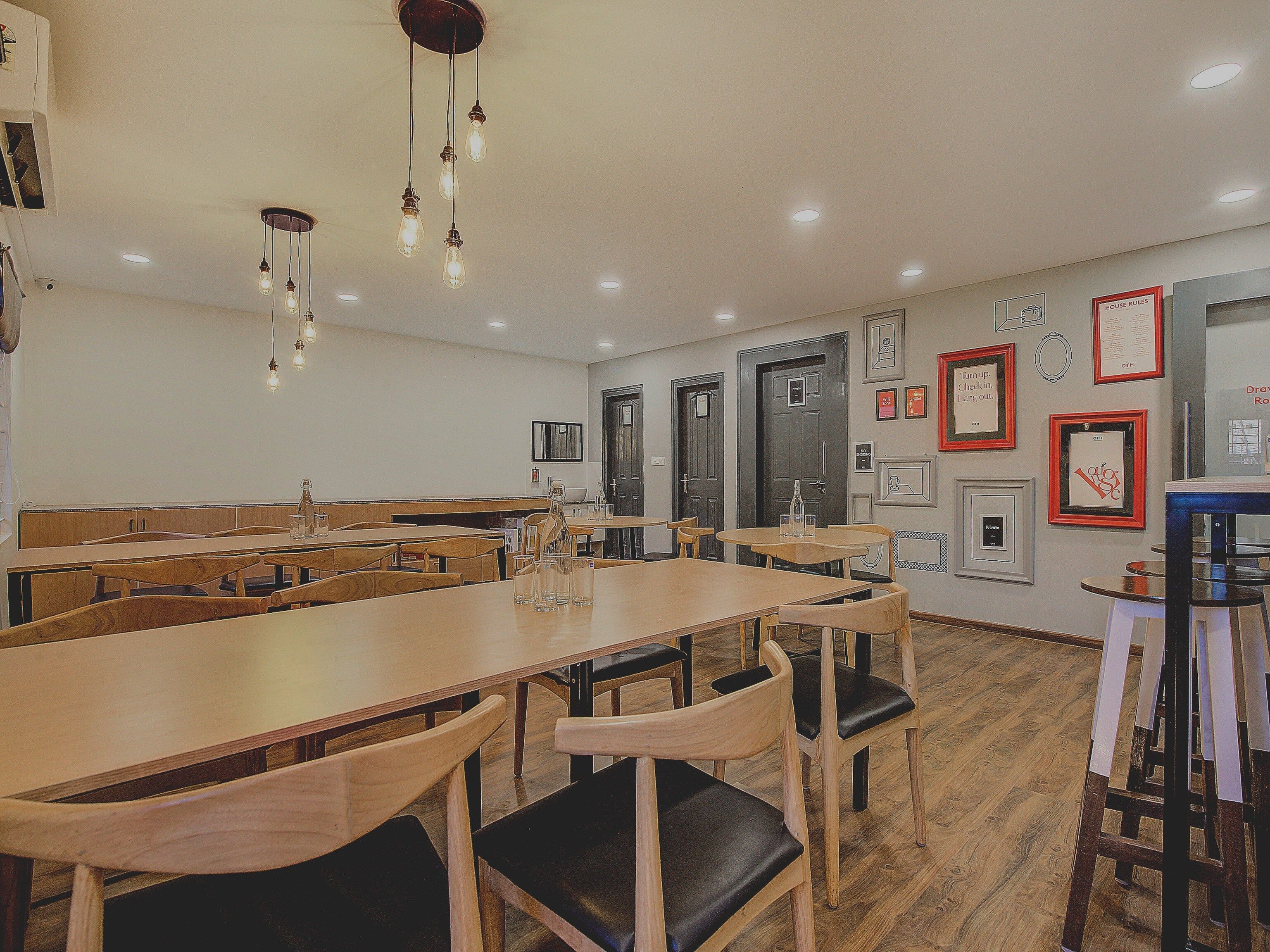 A dining area with wooden tables and chairs, hanging light fixtures, and framed artwork on the walls.