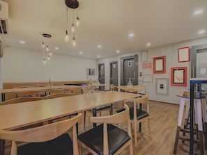 Un comedor con mesas y sillas de madera, lámparas colgantes y cuadros en las paredes.