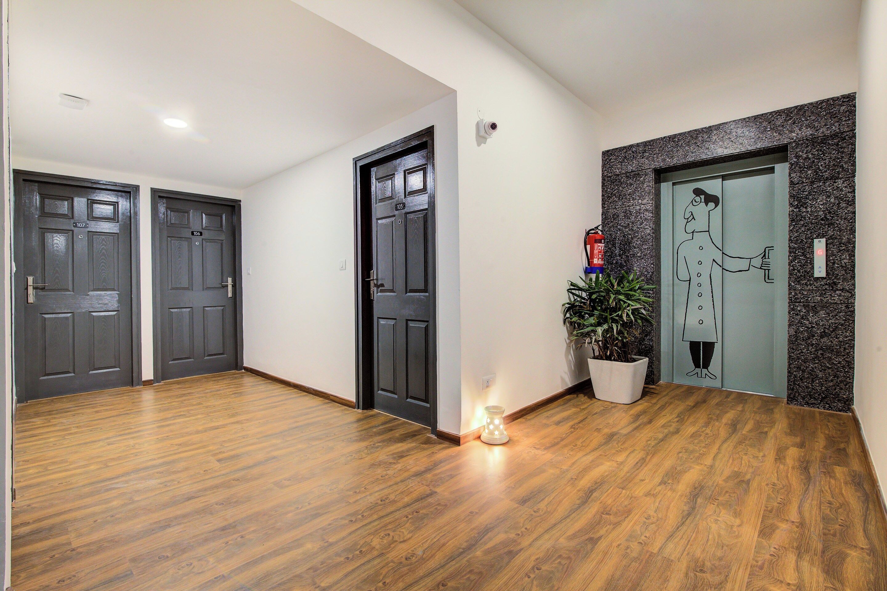 A hallway with wooden flooring, two dark wooden doors, a potted plant, and a fire extinguisher.