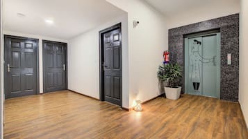 A hallway with wooden flooring, two dark wooden doors, a potted plant, and a fire extinguisher.