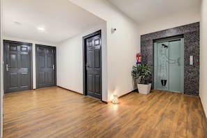 Un pasillo con piso de madera, dos puertas de madera oscura, una planta en maceta y un extintor.
