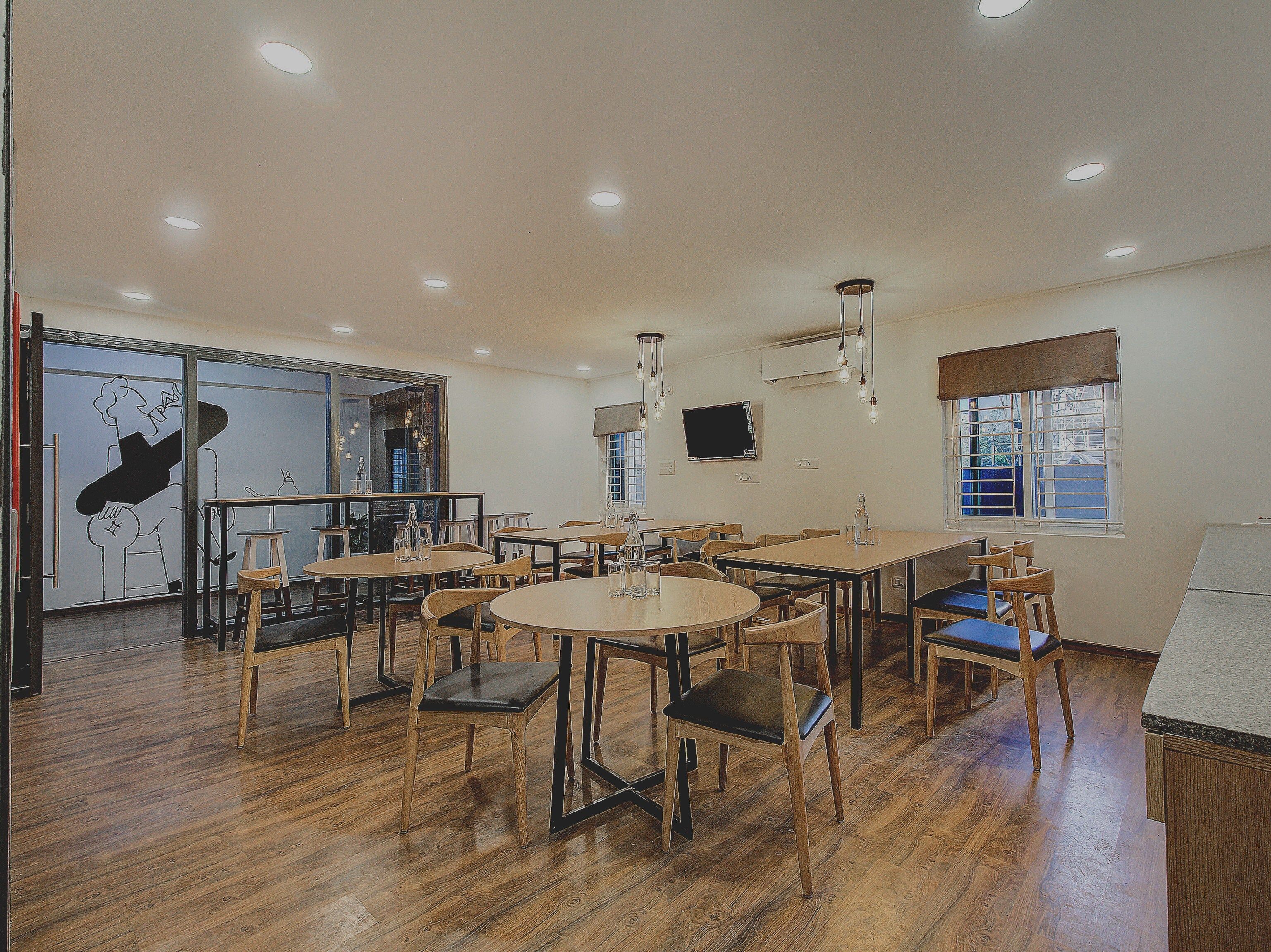 A dining area with multiple tables and chairs, wooden flooring, and recessed ceiling lighting.