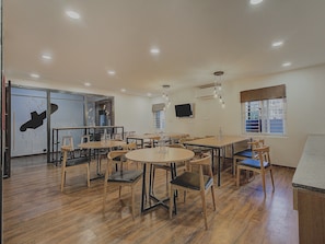 A dining area with multiple tables and chairs, wooden flooring, and recessed ceiling lighting. - Hotel O Evergreen (Faridabad)