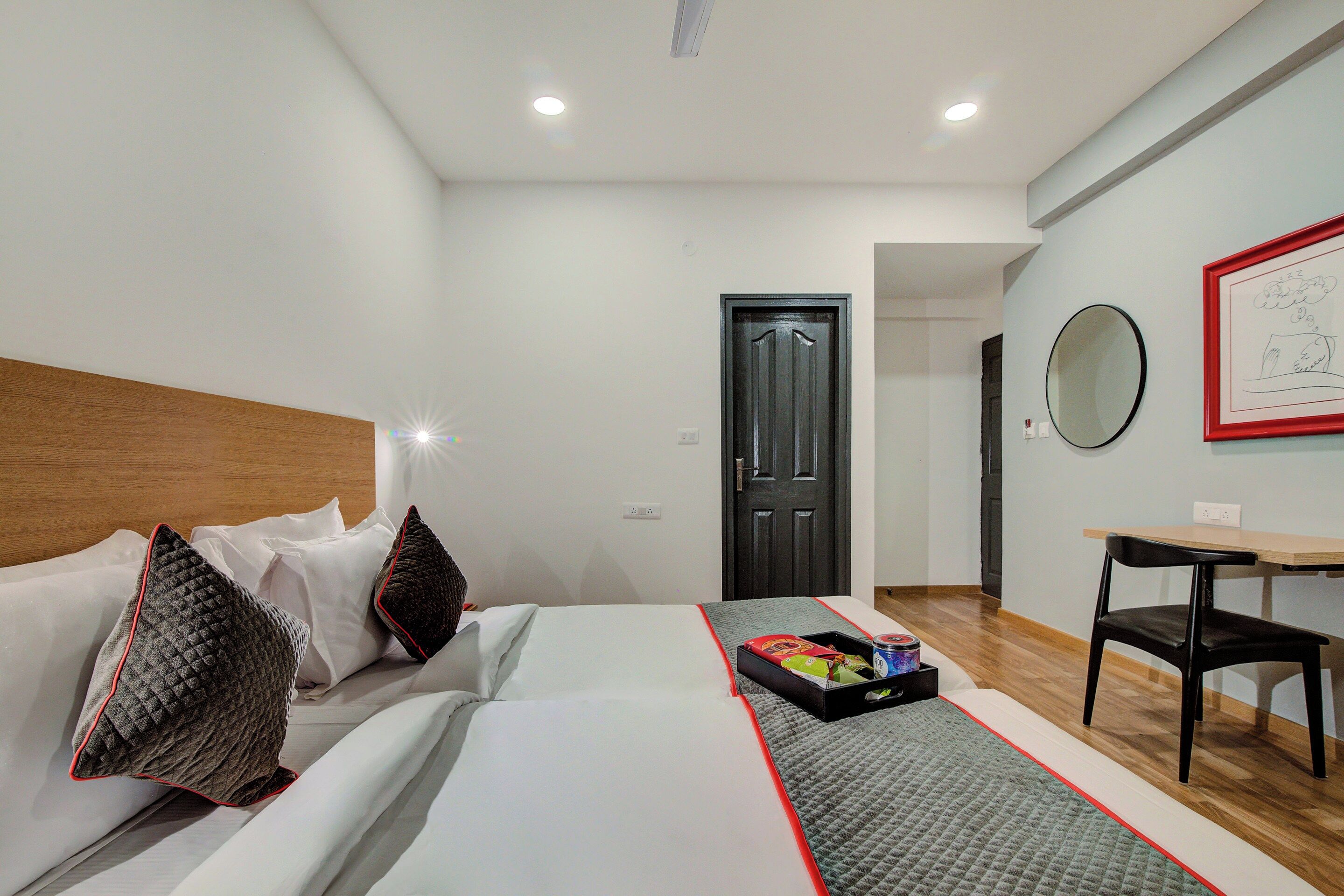 A hotel room with a bed, a desk, a chair, a door, and a wall with a framed picture.