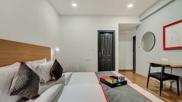 A hotel room with a bed, a desk, a chair, a door, and a wall with a framed picture.