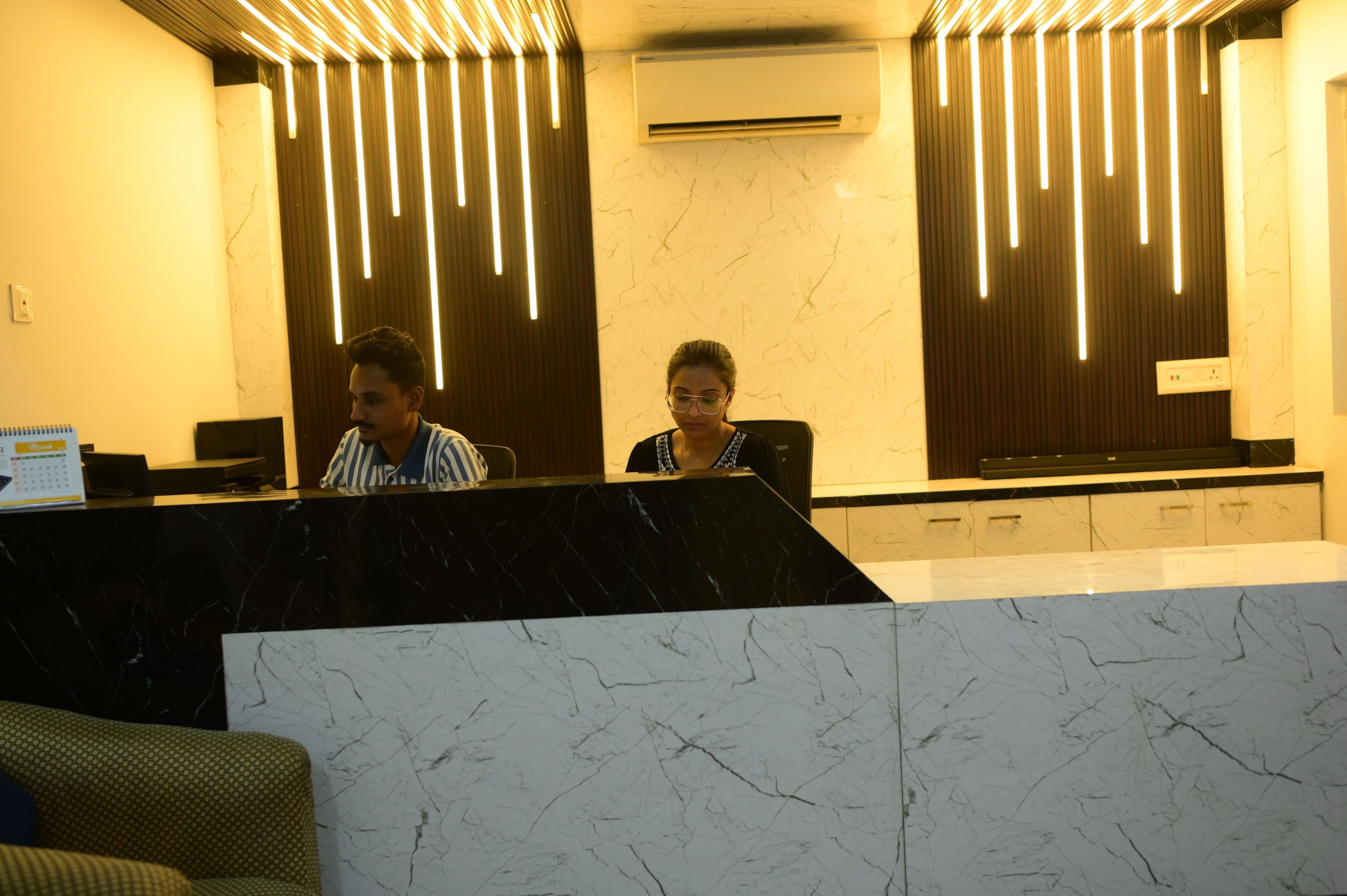 A reception desk with a marble top, a wall-mounted air conditioner, and vertical light fixtures.