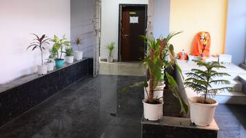 A hallway with potted plants, a reception desk, and a door leading to another room.