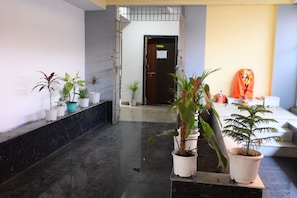 Un passadís amb plantes en testos, una recepció i una porta que condueix a una altra habitació.