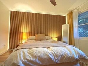 Un dormitori amb un llit, làmpades de nit, una finestra amb cortines i un ventilador de sostre.