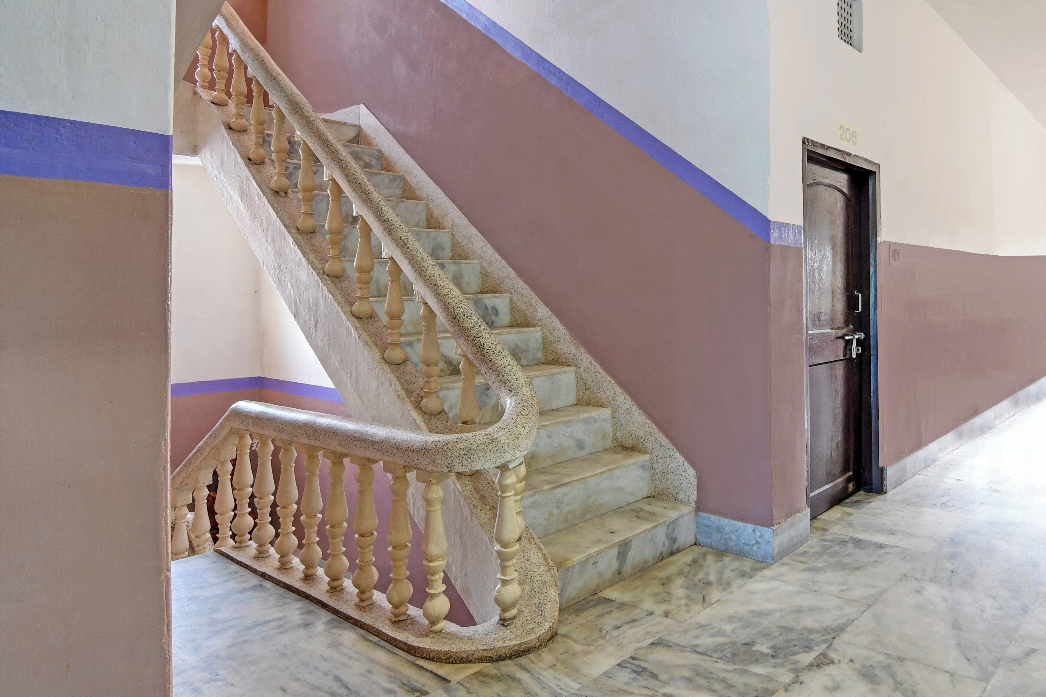 Un escalier avec des marches et des balustrades en marbre, menant à une porte dotée d’une poignée en métal.
