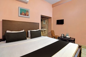 Een hotelkamer met een bed, een stoel, een klein tafeltje met een waterkoker en een televisie aan de muur.