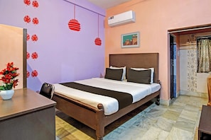 Een hotelkamer met een bed, een bureau, een potplant en een luchtverkoeler aan de muur.