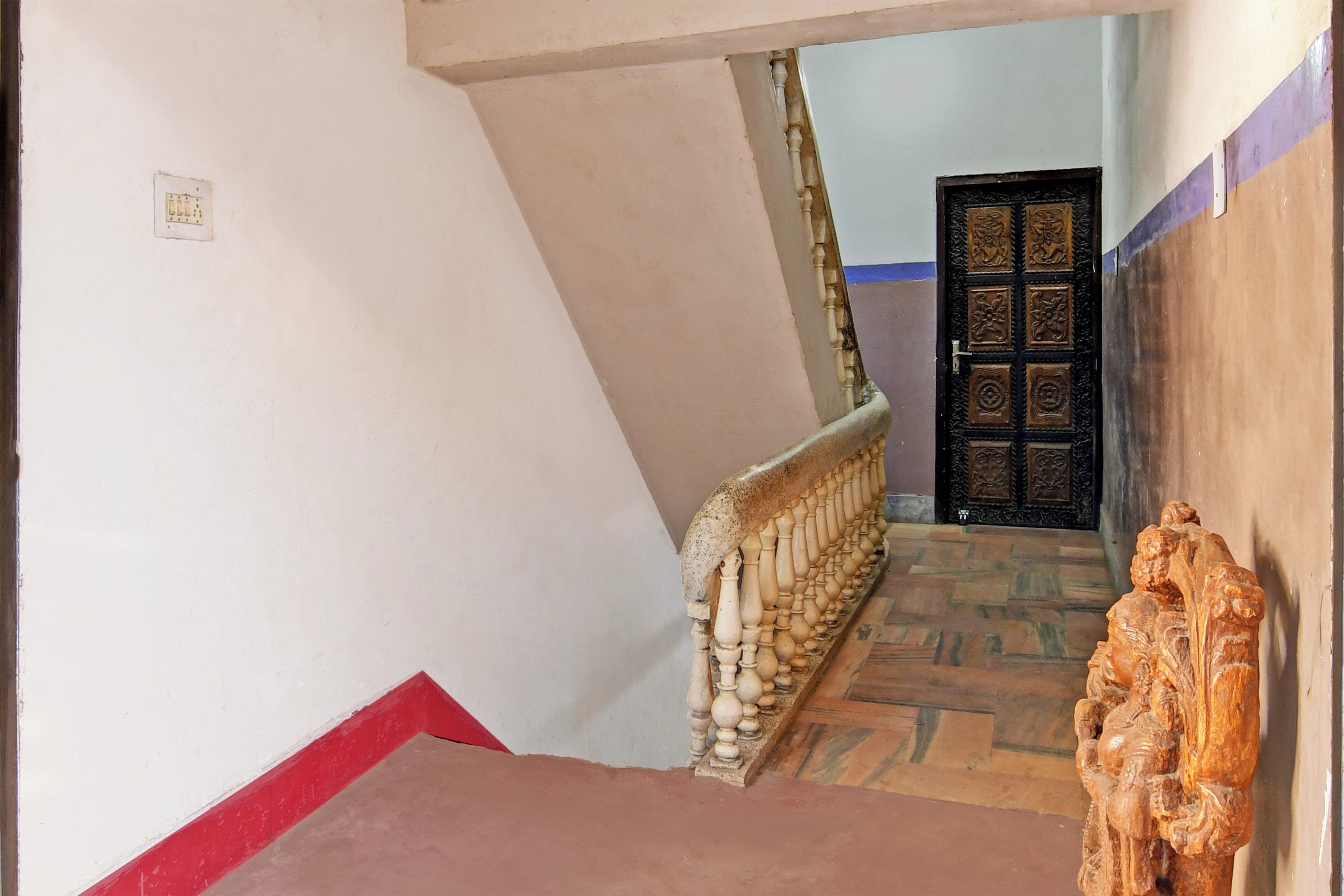 Una escalera con barandilla, una puerta con tallado intrincado y una pared con interruptor de luz.