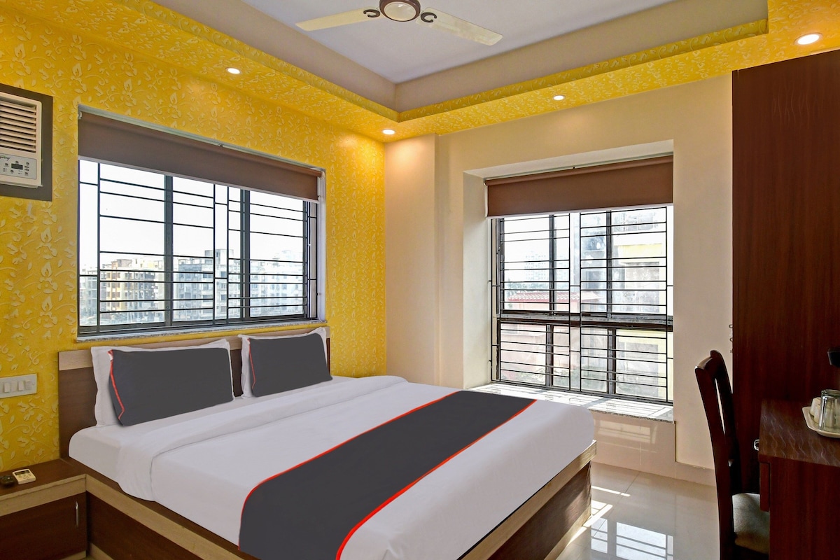 A hotel room with a bed, two windows, a ceiling fan, and a view of the cityscape.