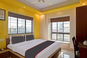 A hotel room with a bed, two windows, a ceiling fan, and a view of the cityscape. - Hotel O Comfort N Cozy (Kolkata)