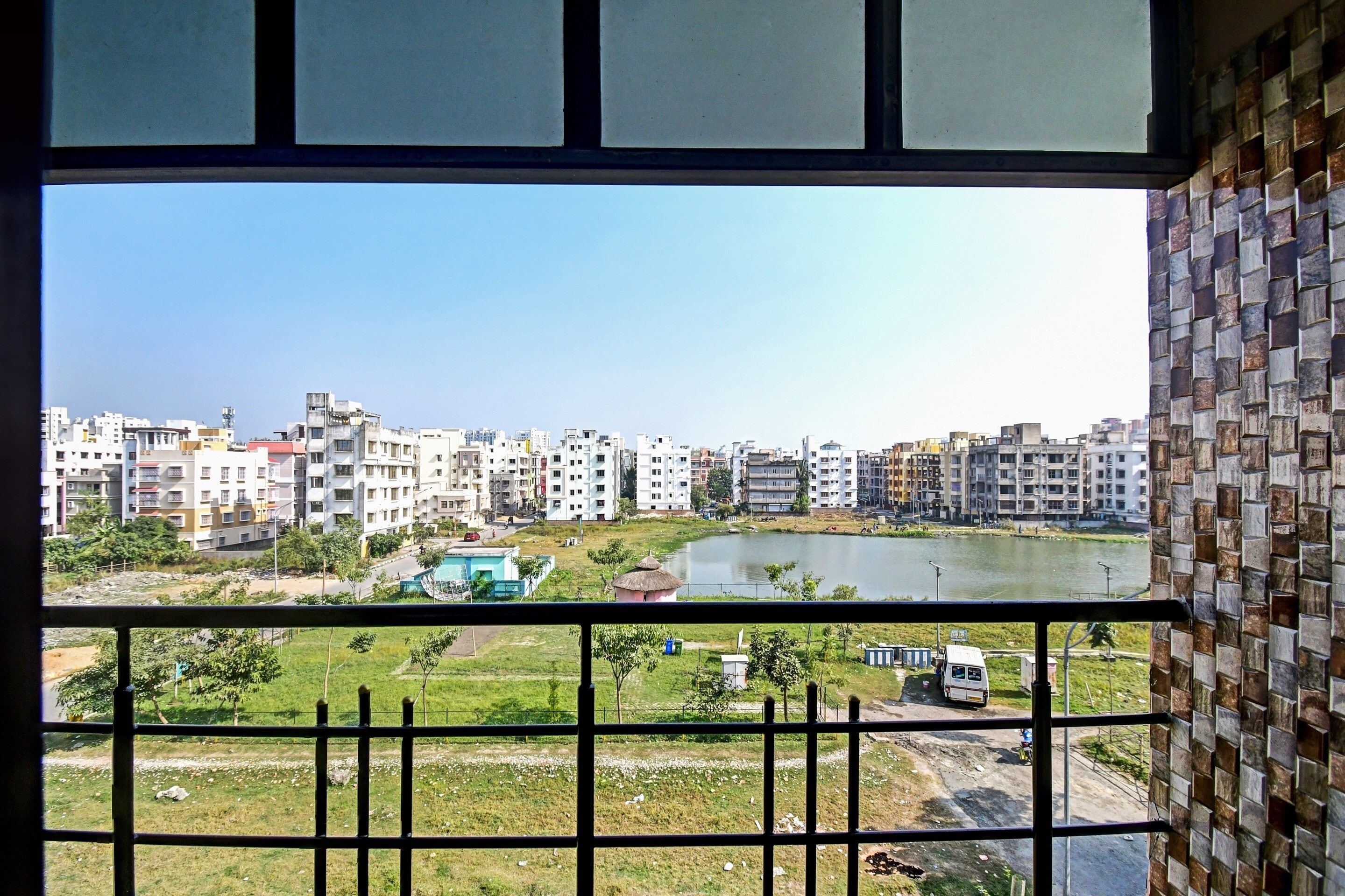 A view from a window overlooking a cityscape with buildings, a body of water, and a green area with a fence.