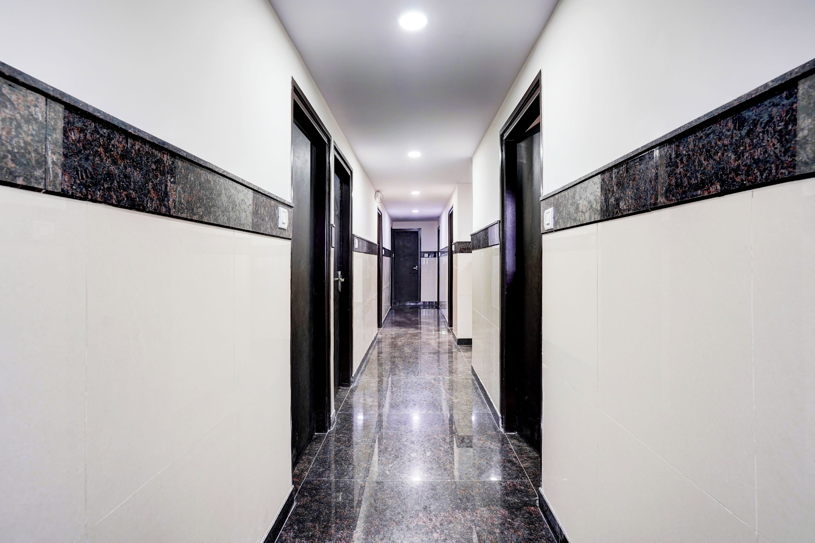 A corridor with a polished floor, white walls, and black doors.