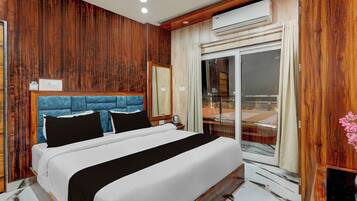 Habitación de hotel con pared de madera, cama con cabecera azul, unidad de aire acondicionado y un ventanal con vistas.