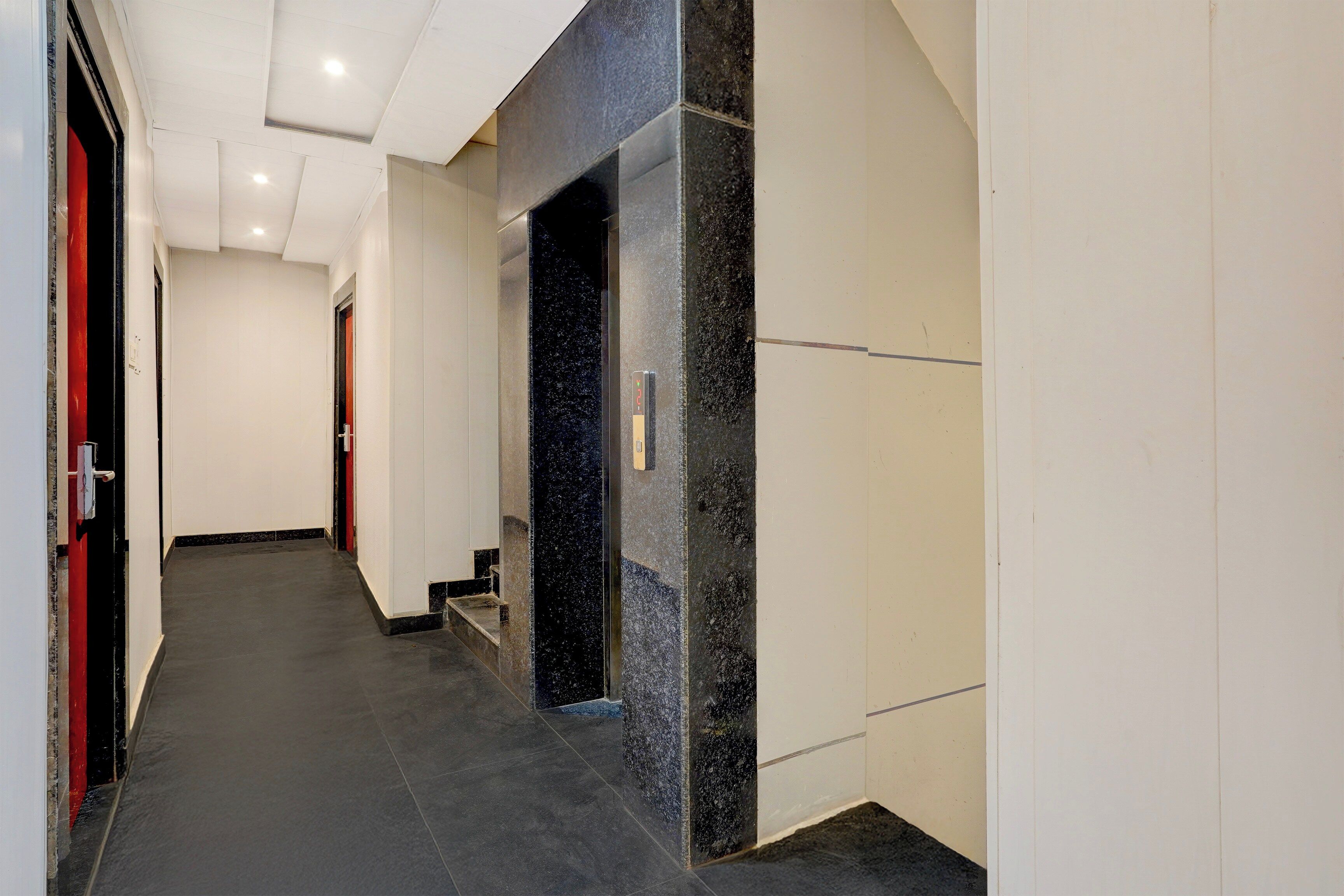 Un pasillo con una pared de mármol negro, una puerta con picaporte rojo y una escalera que conduce a un nivel superior.