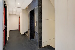 Um corredor com parede de mármore preto, porta com puxador vermelho e escada que leva a um andar superior.