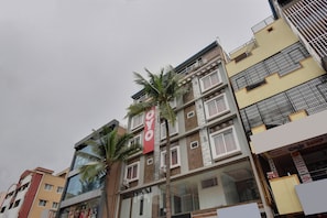 Un edificio de varios pisos con un llamativo letrero rojo en la fachada, varios balcones y una palmera en frente.