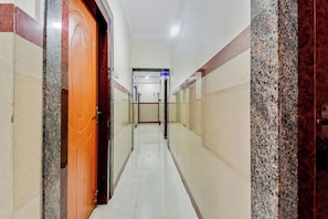 Un pasillo con una puerta de madera a la izquierda, paredes y piso de baldosas.