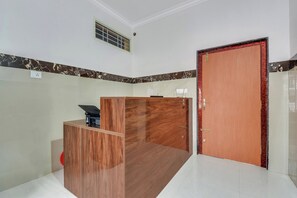 Una habitación con un mostrador de recepción de madera, una puerta con marco rojo y suelo de baldosas.