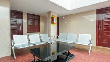 Un área de espera con una mesa de vidrio y sillas blancas, paredes de mármol y dos puertas con los números 104 y 102.