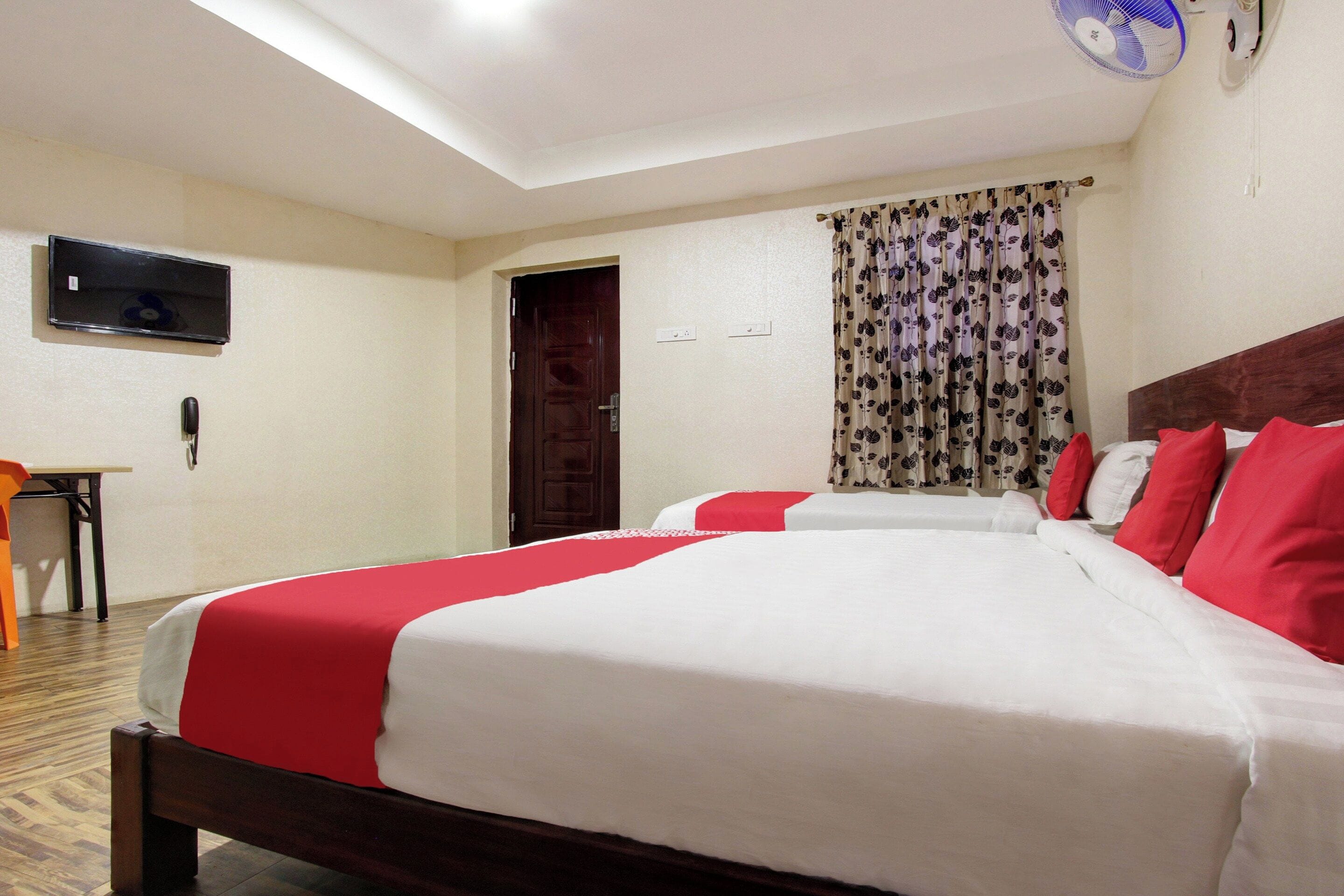 A hotel room with two beds, a television on the wall, a desk, and a door.