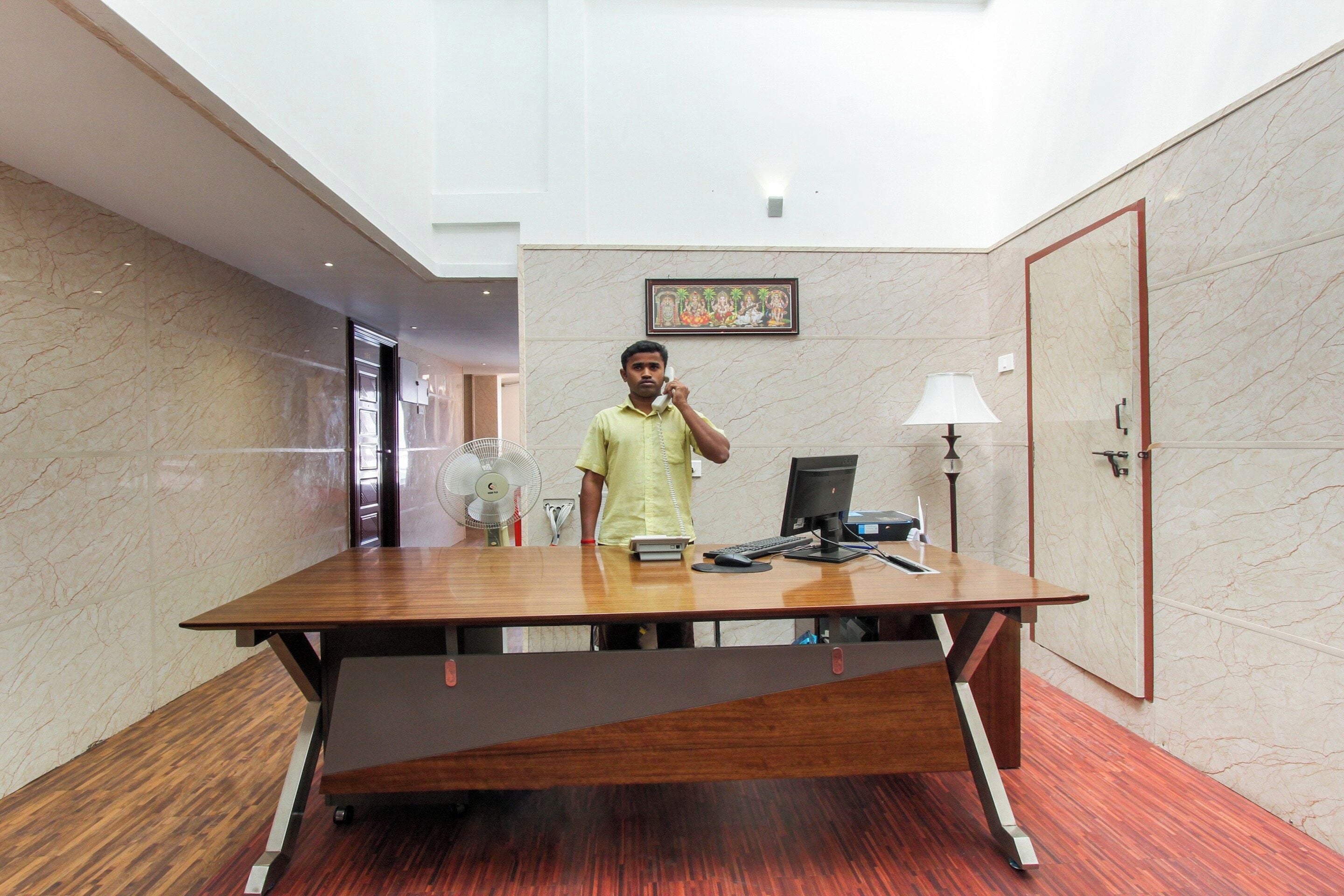 A hotel room with a wooden desk, a computer, a lamp, and a framed artwork on the wall.