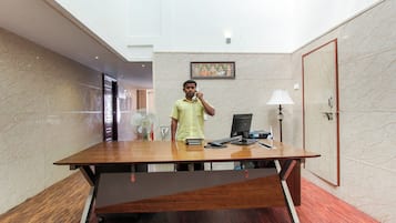 A hotel room with a wooden desk, a computer, a lamp, and a framed artwork on the wall.