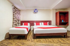 A hotel room with two beds, a wooden floor, a ceiling fan, and a small shelf with a water bottle. - Super Hotel O Am Grandd (Trichy)