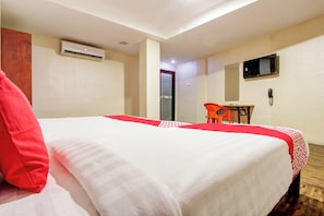A hotel room with a bed, a desk, a chair, an air conditioning unit, and a television. - Super Hotel O Am Grandd (Trichy)