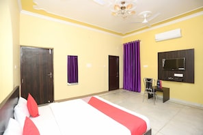 A hotel room with a bed, a desk, a chair, a TV, and a ceiling fan. - Hotel O Greenview Near Munshi Pulia (Lucknow)