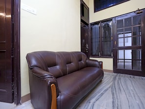 Un sofá de cuero marrón oscuro en una habitación con piso de mármol, una puerta de madera oscura y una ventana con barrotes.